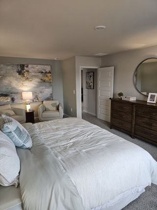 A cozy bedroom with a plush bed, abstract artwork, soft lighting, and elegant wooden dresser.