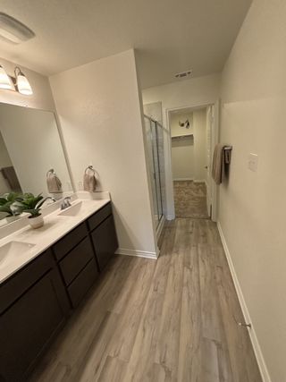 A modern bathroom with dual sinks, wood-look flooring, a large mirror, and a glass shower enclosure.