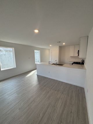An open living space with sleek gray flooring, recessed lighting, and a modern kitchen in a fresh, minimalist style.