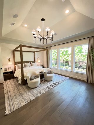 Model Home A spacious bedroom with a wooden canopy bed, plush chairs, and large windows overlooking greenery.