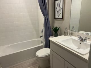 A contemporary bathroom with a sleek white vanity, elegant framed art, and a cozy bathtub with curtain.