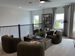 A cozy loft with green armchairs, a wooden coffee table, elegant shelving, and soft lighting from large windows.
