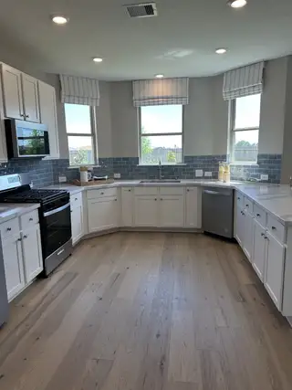 A spacious kitchen with white cabinets, stainless appliances, light wood flooring, and elegant blue tile backsplash.