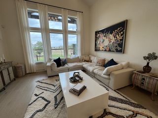 A bright living room with a large window, cozy sectional sofa, patterned rug, and vibrant floral artwork.