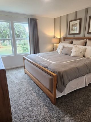 A cozy bedroom with a wood-framed bed, soft gray bedding, and large windows overlooking a lush garden.