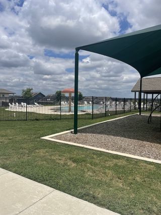 Community Amenities A sunny view of the Knox Ridge community pool and playground by Lennar (Converse, TX), featuring a shaded play area and fenced pool with lounge chairs.