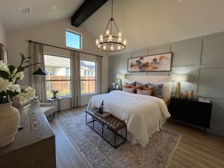 A luxurious primary bedroom with vaulted ceilings, warm decor, and a statement chandelier in Solterra by David Weekley Homes (Mesquite, TX).