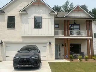 A modern two-story home with white brick, wooden columns, and a landscaped yard in The Overlook at Factory Shoals by Kerley Family Homes (Mableton, GA).