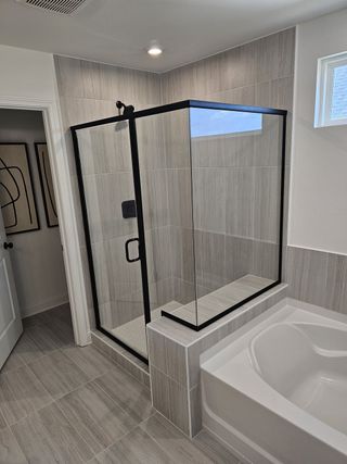 Model Home A modern bathroom with a glass-enclosed shower, sleek tile, and a spacious bathtub, creating a serene retreat.