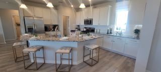 Model Home A modern kitchen featuring granite countertops, white cabinetry, and stylish bar stools, illuminated by chic pendant lighting.
