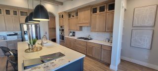 A modern kitchen featuring wood cabinetry, an island with gold fixtures, and stylish pendant lighting.