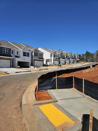 A row of contemporary homes line a sunny street in Waypoint by D.R. Horton, Flowery Branch, GA, under a clear blue sky.