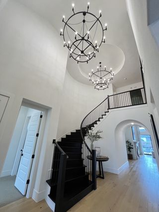 Model Home A grand foyer featuring elegant black staircase, modern chandeliers, and bright wood flooring for a luxurious entryway.
