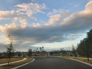 A serene road in Jennings Farm by Dream Finders Homes, Middleburg, FL, with lush greenery and a picturesque sky.