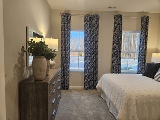 A cozy bedroom with patterned curtains, a soft carpet, and a wooden dresser adorned with decorative vases and a lamp.