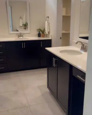 A modern bathroom featuring sleek dark cabinets, double sinks, and minimalist decor.