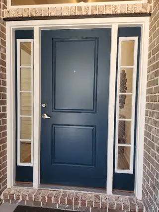 A navy front door with sidelights and brick surround offers a warm, inviting entrance.