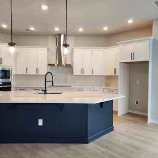 A modern kitchen with a large island, white cabinets, and stainless steel hood, enhanced by elegant pendant lighting.