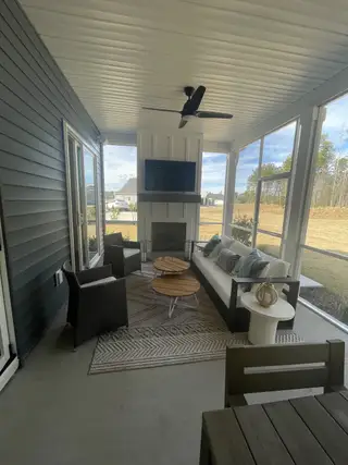 Model Home A cozy screened porch with elegant seating, a rustic coffee table, and a ceiling fan, perfect for relaxation.