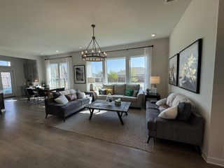 Model Home A cozy living room with large windows, soft gray sofas, rustic coffee table, and contemporary artwork. Bright, open space.