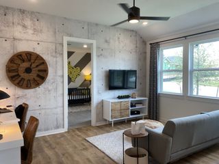 Model Home A modern living space with a faux concrete wall, cozy seating, and sleek decor, accented by a large rustic wall clock.