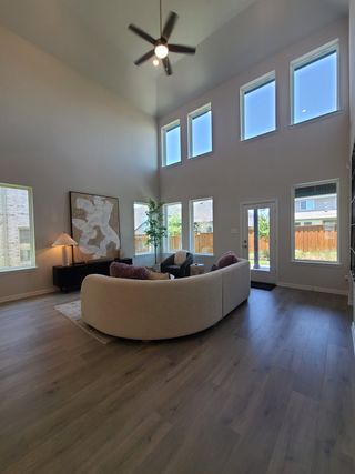 A spacious living room with a vaulted ceiling, large windows, elegant artwork, and a cozy curved sofa arrangement.