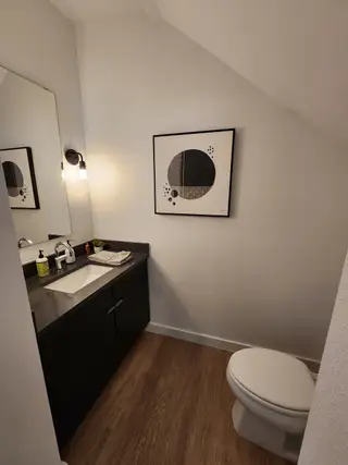 A sleek powder room with a dark vanity, modern lighting, and stylish artwork, featuring wood flooring for a contemporary touch.