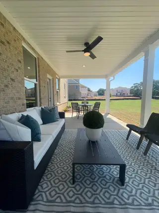 A cozy outdoor patio with elegant seating, a stylish rug, and a ceiling fan for relaxation and comfort.