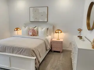 A cozy bedroom with a plush bed, soft lighting, and stylish decor, featuring a pink nightstand and elegant accents.