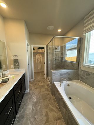 A luxurious primary bathroom with a soaking tub, glass-enclosed shower, and elegant dark cabinetry with dual sinks.
