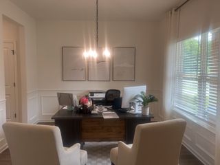 A cozy home office with elegant seating, a wooden desk, chic lighting, and natural light streaming through the window blinds.
