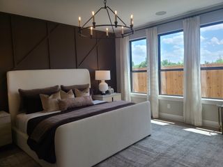 A cozy bedroom with a modern chandelier, dark accent wall, elegant white bed, and large windows letting in natural light.