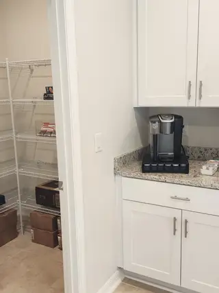 A modern pantry with wire shelving, granite countertops, and a sleek coffee maker for a functional kitchen space.