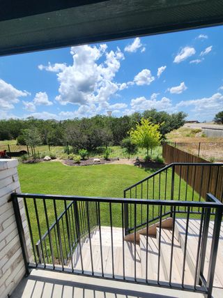A covered patio with a scenic view of a lush green backyard and black metal railing.