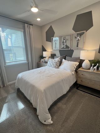 Model Home A cozy bedroom featuring geometric accent walls, plush bedding, and giraffe-themed artwork, illuminated by stylish lighting.
