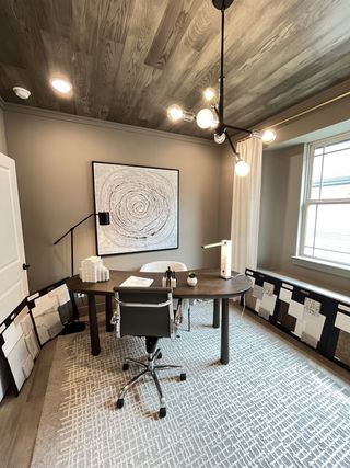 Model Home A modern office with wood ceiling, abstract art, sleek furniture, and stylish lighting, creating an inviting workspace.