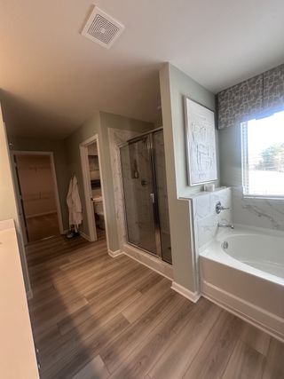 A spacious master bathroom with a glass shower, large tub, and light wood flooring in Dacula, GA.