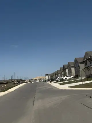 Street view A sunny street view of Magnolia Village (San Antonio, TX) by Rosehaven Homes features modern townhomes lining the street under a clear blue sky.