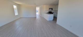 Model Home An open-concept living space with light wood flooring and a modern kitchen, featuring white cabinetry and sleek countertops.
