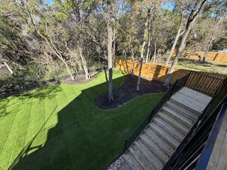 Model Home A beautifully landscaped backyard with lush grass, trees, and wooden fencing, featuring a descending staircase.