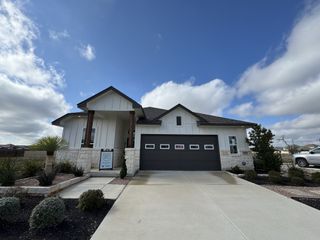 Street view A charming white modern ranch home with stone accents in August Fields by Chesmar Homes (New Braunfels, TX).