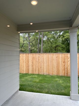A cozy patio with recessed lighting and a view of a lush green yard, enclosed by a wooden fence for privacy.
