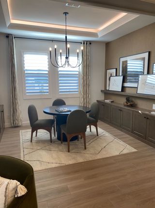A stylish dining area features a round black table with gray upholstered chairs, a modern chandelier, and a built-in buffet with artwork display.