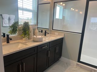 A modern bathroom featuring dual sinks with black fixtures, marble countertops, and large windows for natural light.