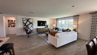 A spacious living room with a white sofa, modern art, and large windows allowing natural light to flood the space.