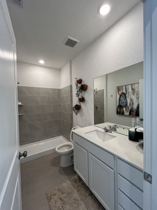 A modern bathroom with a large mirror, white vanity, and gray tiled shower, complemented by decorative wall plants.
