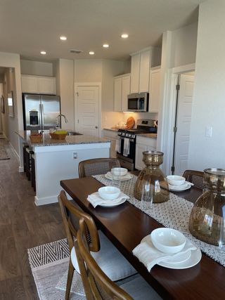A stylish dining area with a modern table setting, leading to an open kitchen with white cabinetry, in a Hunters Ranch home by View Homes (San Antonio, TX).