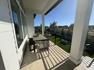 Model Home A charming outdoor patio with a dining set, overlooking lush greenery under a clear blue sky.