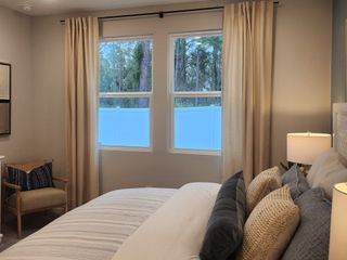 A cozy bedroom featuring soft, neutral tones, elegant curtains, plush pillows, and natural light from large windows.