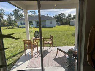 A cozy patio area featuring wooden furniture, a patterned rug, and serene green views through sliding doors.